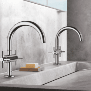 Close-up of two modern Grohe chrome faucets with high-arch spouts and cross handles on a gray concrete integrated sink.