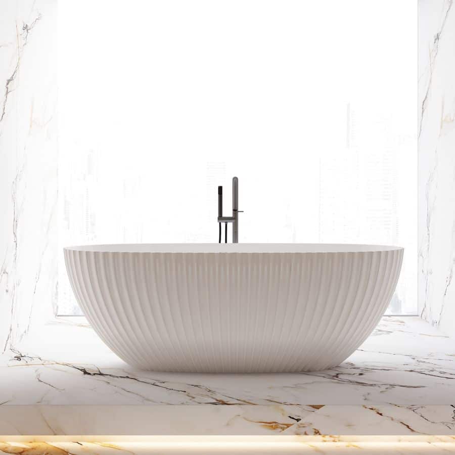 White fluted acrylic freestanding tub with a modern floor-mount faucet on a white and gold marble floor.