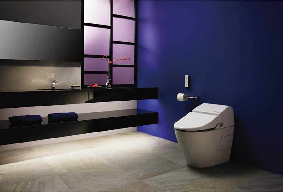 Modern white Toto Washlet toilet with wall-mounted remote, set against a deep blue wall next to a sleek black floating vanity.