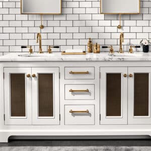 White double vanity with marble top, gold faucets, and bronze mesh cabinet doors against a white subway tile backsplash.